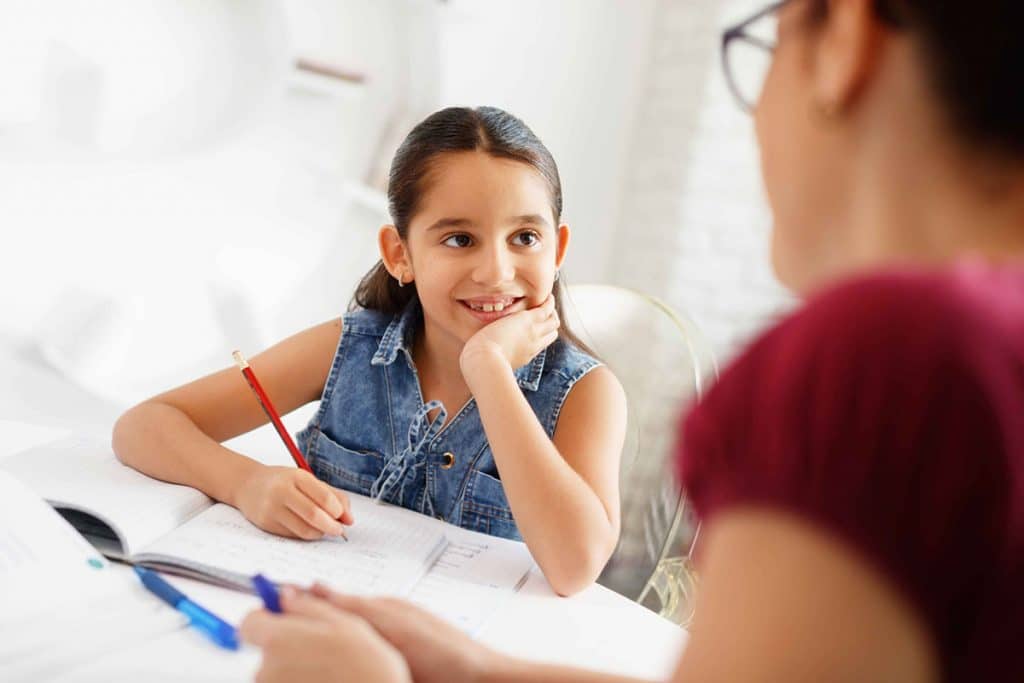 Hispanic Mother Helping Girl Doing School Homework At Home